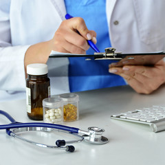 Medical Doctor writes a prescription of medicine. Pills in bottles and stethoscope. Medical office in a clinic. Physician holds a clipboard. Medical content. Healthcare. Treatment. Pharmacy.