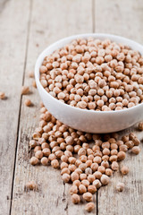 Fresh raw organic chickpeas in white ceramic bowl on rustic wooden table background.