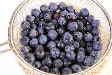 Fresh blueberries in wire mesh strainer with water drops as they drain from washing.