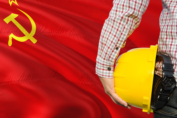 Engineer is holding yellow safety helmet with waving Soviet Union flag background. Construction and...