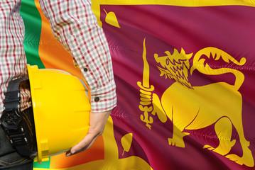 Sri Lankan Engineer is holding yellow safety helmet with waving Sri Lanka flag background. Construction and building concept.