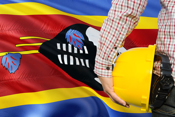 Swazi Engineer is holding yellow safety helmet with waving Swaziland flag background. Construction...