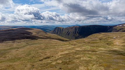 An aerial view of a Scottish mountain cliff with heather in the foreground under a majestic blue...