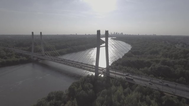 Flying over the river hung through a busy road. Warsaw downtown on the background at sunset. Panoramic aerial view of Warsaw Siekierkowski Bridge with the river in the background. 4K drone in RAW.