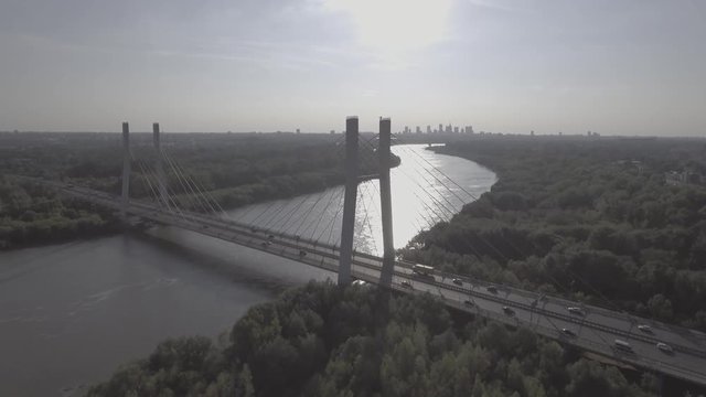Flying over the river hung through a busy road. Warsaw downtown on the background at sunset. Panoramic aerial view of Warsaw Siekierkowski Bridge with the river in the background. 4K drone in RAW.