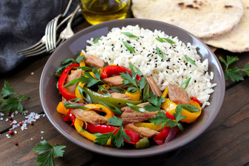 Stir-fry sweet pepper with beef served with rice and naan bread on dark background. Top view with copy space. Asian food.