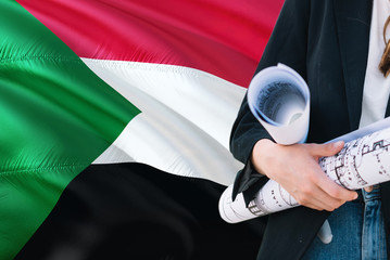 Sudanese Architect woman holding blueprint against Sudan waving flag background. Construction and architecture concept.