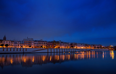 Fototapeta na wymiar Houses on Betis street to Isabel bridge Seville reflected at dawn in Alfonso XIII Canal