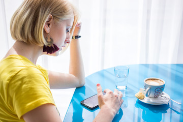 Girl in yellow t-shirt looking at her phone. Inside a coffee shop.