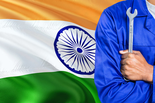 Indian Mechanic in blue uniform is holding wrench against waving India flag background. Crossed arms technician.