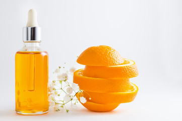 Vitamin C serum in cosmetic bottle with dropper, sliced orange and flowers on white background. Organic SPA cosmetics with herbal ingredients.