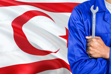 Turkish Mechanic in blue uniform is holding wrench against waving Northern Cyprus flag background. Crossed arms technician.