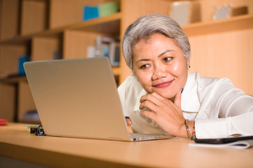 Fototapeta na wymiar lifestyle office portrait of attractive and happy successful middle aged Asian woman working at laptop computer desk smiling confident in entrepreneur business success