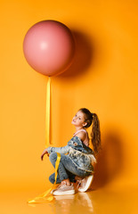 Young beautiful teenager girl posing on a yellow background, lies and holds up a huge giant pink balloon. Summer style.