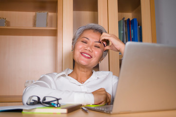 Fototapeta na wymiar natural lifestyle office portrait of attractive and happy successful mature Asian woman working at laptop computer desk smiling confident in entrepreneur success