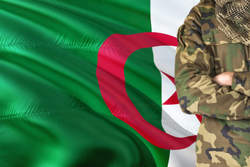 Crossed arms Algerian soldier with national waving flag on background - Algeria Military theme.