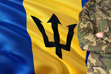 Crossed arms Barbadian soldier with national waving flag on background - Barbados Military theme.