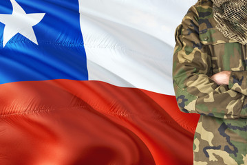 Fototapeta na wymiar Crossed arms Chilean soldier with national waving flag on background - Chile Military theme.