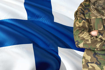 Crossed arms Finnish soldier with national waving flag on background - Finland Military theme.