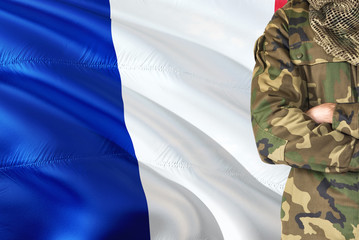 Crossed arms French soldier with national waving flag on background - France Military theme.