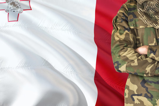 Crossed arms Maltese soldier with national waving flag on background - Malta Military theme.