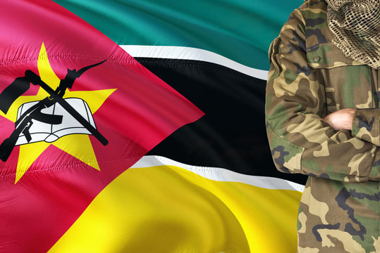 Crossed arms Mozambican soldier with national waving flag on background - Mozambique Military theme.