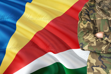 Crossed arms Seychellois soldier with national waving flag on background - Seychelles Military...