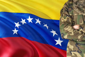 Crossed arms Venezuelan soldier with national waving flag on background - Venezuela Military theme.