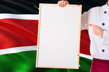 Kenyan Chef holding blank whiteboard menu on Kenya flag background. Cook wearing uniform pointing space for text.