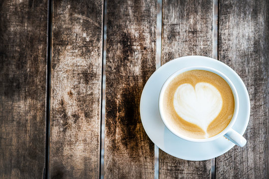 a mug of cappuccino coffee with a painted heart stands on a wooden textured table. top view, close-up. free empty space.
