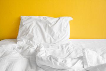 White pillow and with wrinkle messy blanket in bedroom on yellow wall background.