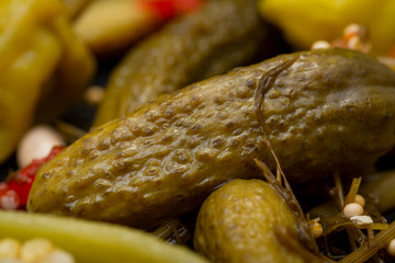 Cornichons (Mini French style Gherkin Cucumbers) and Pickled Pepperoncini Peppers on natural stone background. 