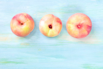 An overhead photo of vibrant organic flat saturn peaches, shot from the top on a teal background...