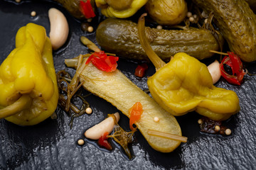 Cornichons (Mini French style Gherkin Cucumbers) and Pickled Pepperoncini Peppers on natural stone background. 