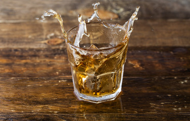 Whiskey splash. Glass of whiskey with ice cubes splashing out.