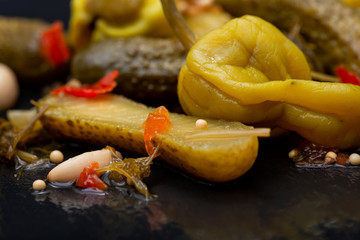 Cornichons (Mini French style Gherkin Cucumbers) and Pickled Pepperoncini Peppers on natural stone background. 