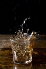 Whiskey splash. Glass of whiskey with ice cubes splashing out.