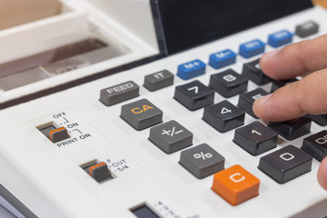 Close-up fingers using calculator to calculate the numbers of monthly expenses and tax at home on wooden table. Finances business savings and accounting concept.