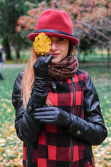 Sensual woman in a red bowler hat with long hair walking in park. Autumn fashion.