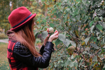 Sensual woman in a red bowler hat with long hair walking in park. Autumn fashion.