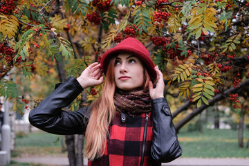 Sensual woman in a red bowler hat with long hair walking in park. Autumn fashion.