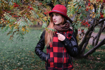 Sensual woman in a red bowler hat with long hair walking in park. Autumn fashion.