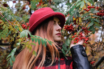 Sensual woman in a red bowler hat with long hair walking in park. Autumn fashion.