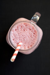 Strawberry banana smoothie in a glass jar mug over black background, overhead view. Top view, from above, flat lay. Close-up.