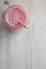 Strawberry banana smoothie in a glass jar mug over white wooden surface, top view. Copy space.