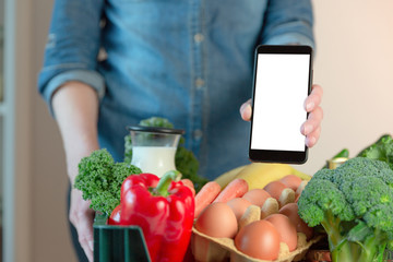 Food delivery service - woman holding smartphone in front of the box of groceries 