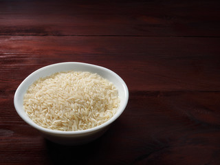 Raw Basmati rice in a white bowl on a brown wooden background