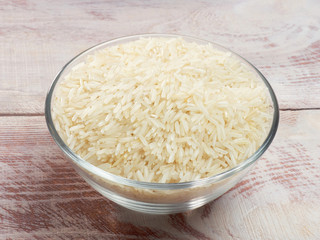 Raw Basmati rice in a glass bowl on a white brown wooden background