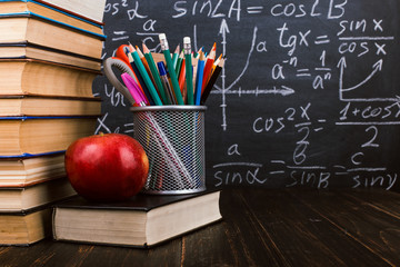 Books, an apple, stand for pens on wooden table, against the background of chalk board with...