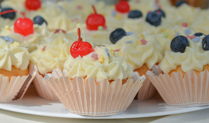Homemade Cupcakes-muffins with cream cheese frosting, decorated with cherry and fresh blueberries. Selective focus